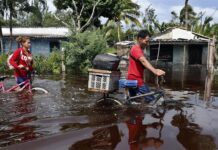 Dos personas caminan con bicicletas por una calle inundada de agua del mar este jueves, tras el paso del huracán Helen
