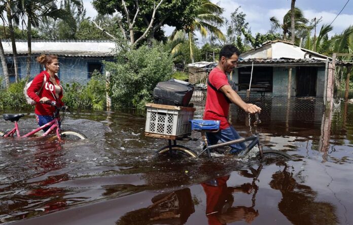 Dos personas caminan con bicicletas por una calle inundada de agua del mar este jueves, tras el paso del huracán Helen