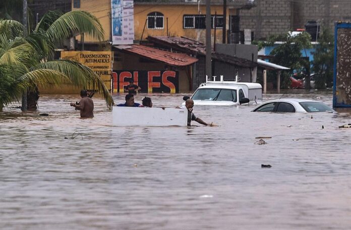 Personas caminan por una calle inundada por el paso del huracán 'John'