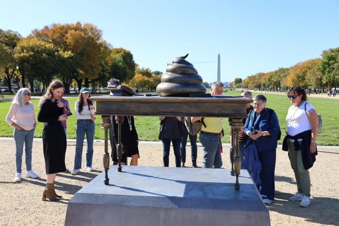 Personas observan una figura en bronce de un escritorio con un excremento encima, instalado en el National Mall cerca del Capitolio Personas observan una figura en bronce de un escritorio con un excremento encima, instalado en el National Mall cerca del Capitolio