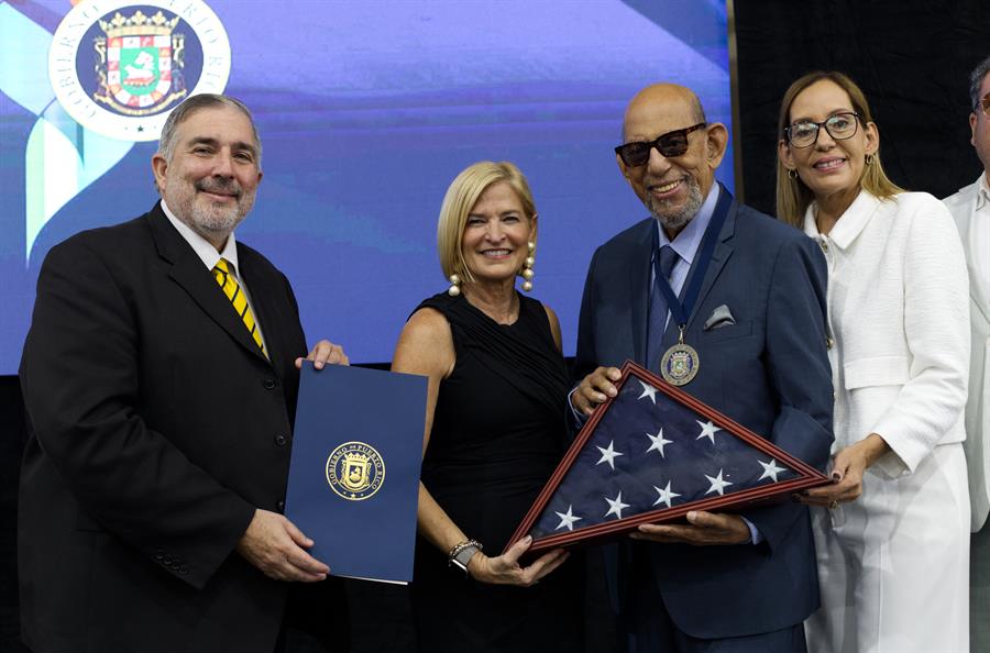 El legendario timbalero Willie Rosario (2d) acompa&ntilde;ado de su hija Elisabeth (d), recibe una bandera de manos de la hermana del Gobernador, Caridad Pierluisis