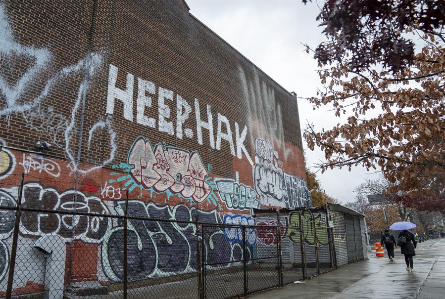 Personas caminan frente a una pared con graffitis este martes en el barrio de Astoria ubicado en el distrito Queens de Nueva York
