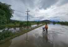 Una persona cruza con su bicicleta por una calle inundada, este domingo en la comunidad de la Sabana, en San Manuel