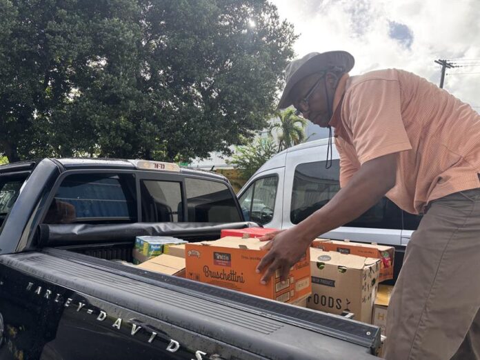 Leonard Phophil carga a un vehículo alimentos que le donan para entregar a los inmigrantes este lunes, en San Juan