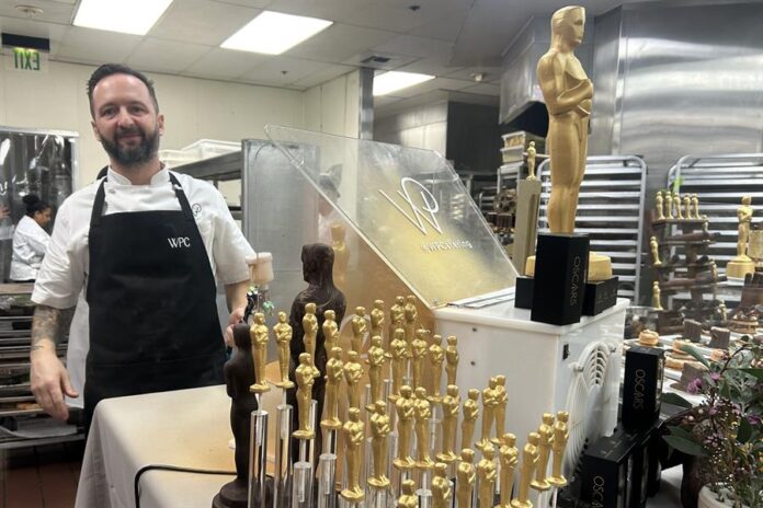 Un ayudante de cocina posa junto a figuras de chocolate de la estatuilla de los premios Oscar Un ayudante de cocina posa junto a figuras de chocolate de la estatuilla de los premios Oscar