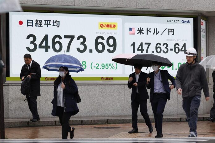Peatones pasan junto a un panel electrónico de la bolsa que muestra el índice Nikkei de Japón
