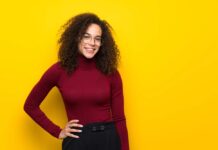 Dominican woman with turtleneck sweater posing with arms at hip and smiling