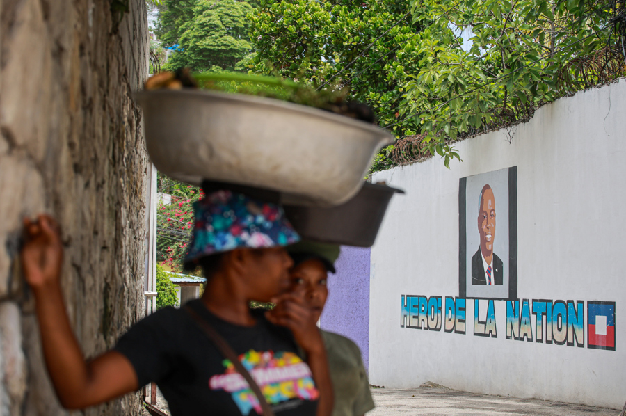  Personas esperan frente a un mural con la imagen del presidente haitiano, Jovenel Mo&iuml;se