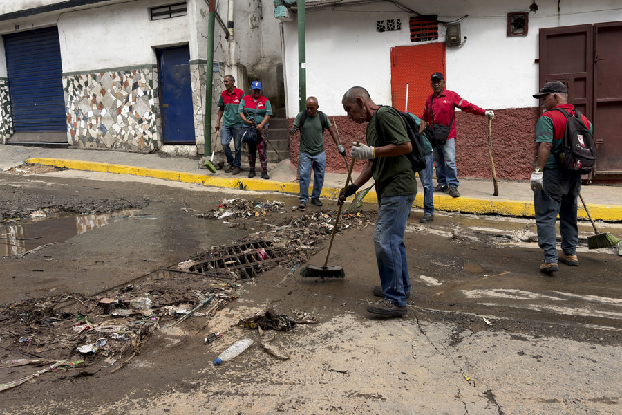 Personas limpian una calle tras las fuertes lluvias este domingo, en Caracas 